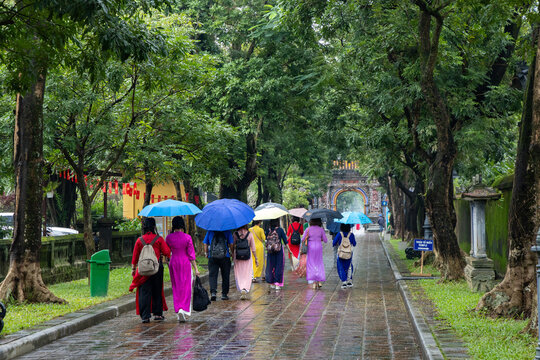 In Hue, Vietnam, women in traditional &Aacute;o d&agrave;i dresses walk with umbrellas in the rain in the Imperial City. They are touring the historic sublocation.
