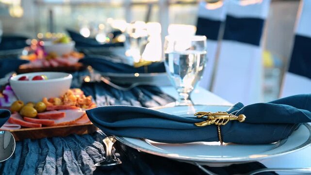 New York, USA, 5 May 2025: Close up of formal table setting with gold lobster napkin ring. Selective focus on a blue fabric napkin with a gold lobster ring next to a meat and cheese platter on a boat.