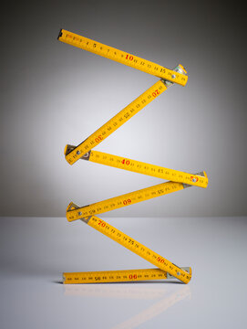 Classic yellow folding wooden carpenter rule balanced vertically in a zigzag shape. Studio shot with a gradient background, concept of precision measurement, craftsmanship, engineering accuracy