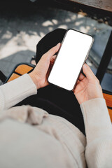 Close-up of hands holding a blank smartphone screen outdoors on a wooden bench, ideal for app mockups, mobile UI design, advertising, and digital marketing concepts.