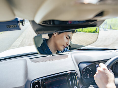 居眠り運転する男性ドライバーのルームミラー越しの表情