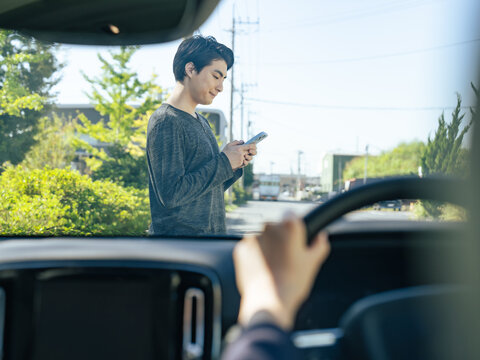 スマホを持って歩いて自動車の前を横断する男性