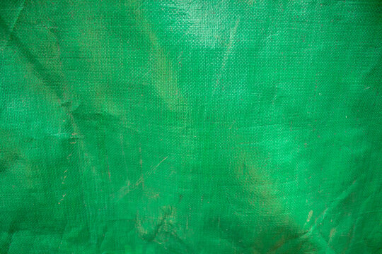 Green plastic tarpaulin with a coarse woven texture and a wrinkled surface.