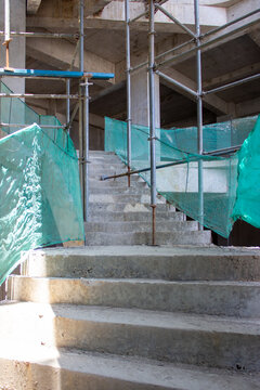 Jakarta, Indonesia - March 16, 2026: Detail of concrete stair access inside construction building with steel pipe scaffolding and green safety net installed neatly
