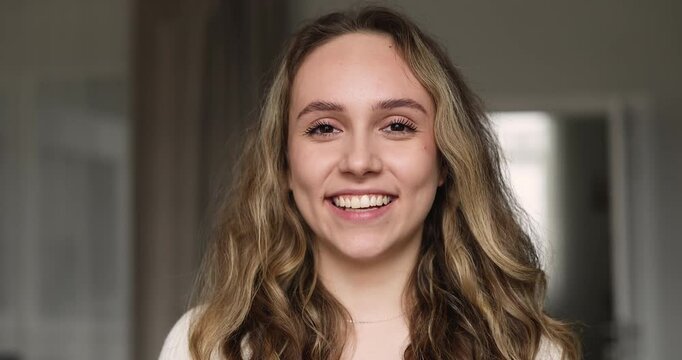 Closeup face, smiling young adult Caucasian woman, posing for home portrait in living room looking at camera, represent confidence, weekend leisure in apartment, personal wellbeing, beauty, positivity