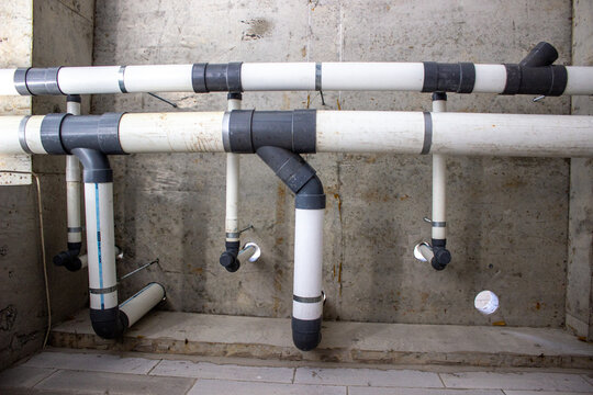 Installation of waste water drainage pipe system details using white PVC pipes with gray fittings on a concrete wall structure.