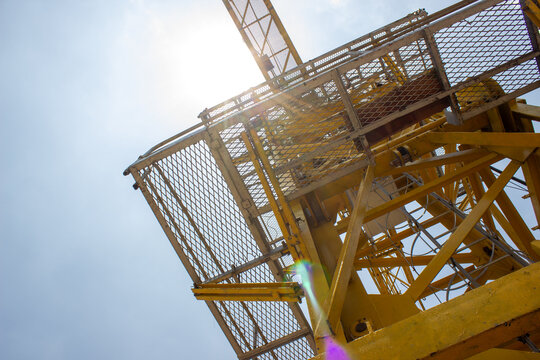 Underside angle of a yellow tower crane structure with metal access platform at a high-rise building construction site