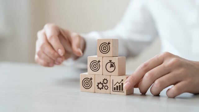 A focused hand carefully stacks wooden blocks featuring business icons, as the camera slowly pans across the scene, capturing the essence of productivity in a cinematic style.