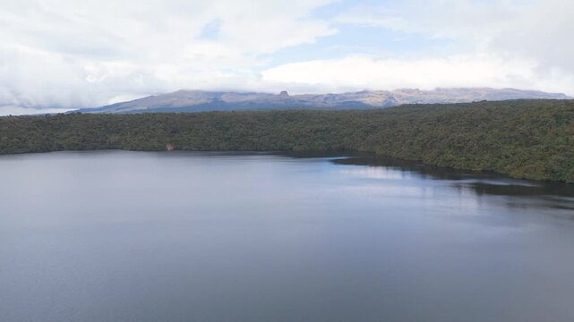 Aerial view of Buey Lagoon with calm waters reflecting green forests under a cloudy sky in Purace National Park, Cauca, Colombia.