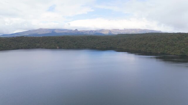 A tranquil view of a lagoon with lush green surroundings and distant mountains under a cloudy sky.