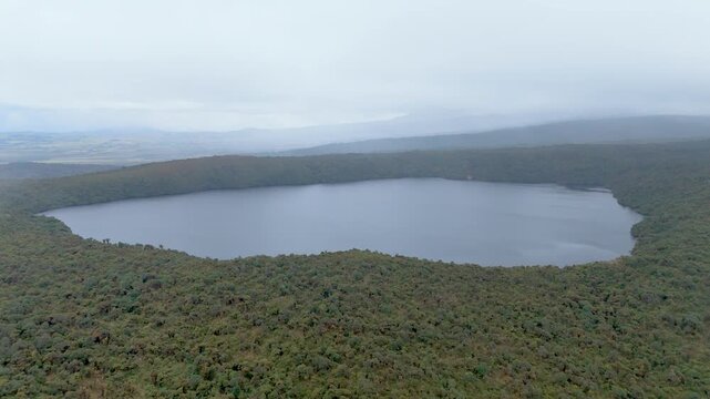 An aerial shot captures the expansive Buey Lagoon surrounded by lush greenery, cloaked in fog, creating a serene atmosphere in Purace National Park.