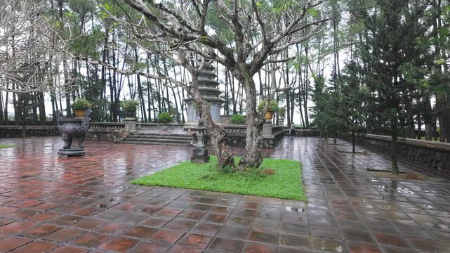 A serene view of the tranquil garden with its bare trees, pagoda, and tiled walkways after a rain shower. Thien Mu Pagoda, Hue, Vietnam.