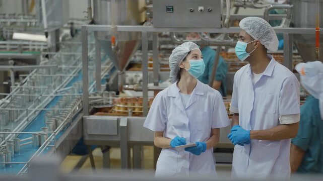 Canned food manufacturing industry, Two quality control officers inspecting products and checking the accuracy of an automated conveyor machine in a processed food production line