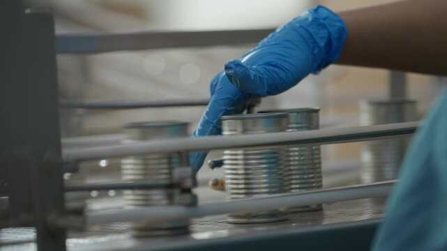 Worker&rsquo;s hand pushing cans quickly along an automated conveyor to prevent machine jams on a canned food production line in a food processing factory