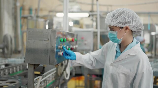 Asian woman worker controlling the control panel of an automated conveyor system in a canned food processing production line at a food manufacturing factory