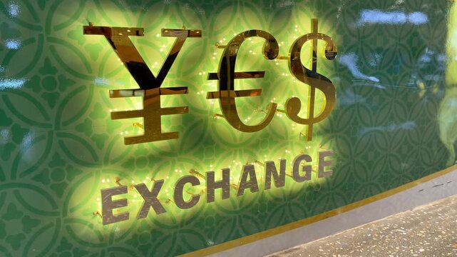 Illuminated currency exchange sign displaying dollar, euro, and yen symbols on a decorative green wall, representing foreign exchange services and international money conversion, Travel abroad concept