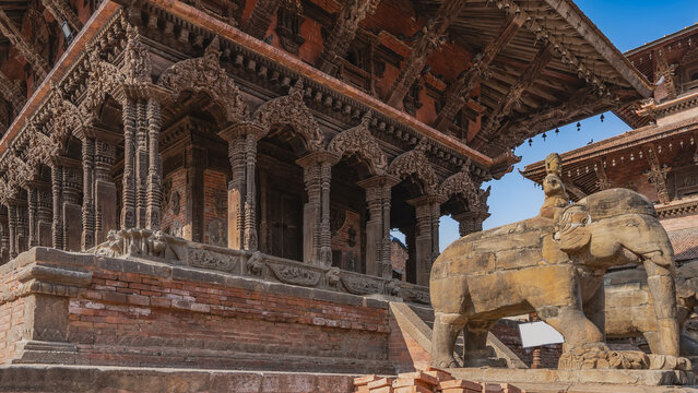 The famous ancient Newar architecture. A temple with carved columns and arches. Stone steps. In the foreground is a sculpture of an elephant with a man on horseback. Nepal. Patan Durbar Square.
 