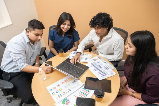 Young indian asian business team entrepreneur meeting in office, discussing company sales reports and financial graphs on a laptop and paper documents, teamwork and professional collaboration.