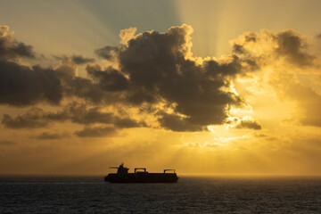 Fototapeta premium Silhouette of a container or tanker ship on the ocean at sunrise or sunset