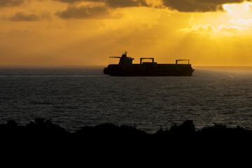 Obraz premium Silhouette of a container or tanker ship on the ocean at sunrise or sunset