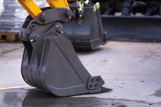 Compact excavator digging bucket resting on concrete at an equipment yard, representing construction workflow, attachment systems and fleet upkeep