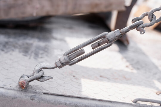 Metal chain tensioner fastened to a transport platform, representing load securing systems, trailer safety and equipment hauling operations
