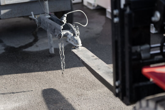 Trailer hitch coupler with safety chain positioned beside forklift forks, highlighting yard logistics, towing setup and equipment handling workflow