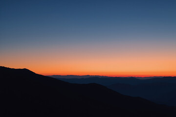 Obraz premium Minimalist sunrise over mountain silhouettes with a smooth gradient sky. Clean modern nature background with large copy space for design, presentations, and website banners.
