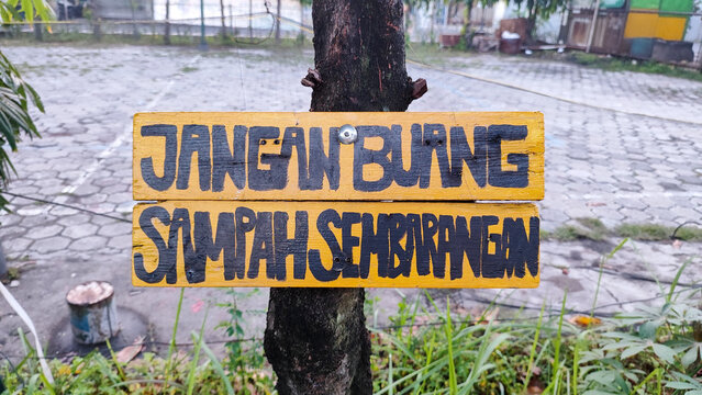 The sign of 'please no littering' on bahasa indonesia called Jangan buang sampah sembarangan. Write on yellow wood sign