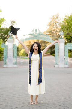 Excited Berkeley graduate celebrating with cap at iconic campus gate