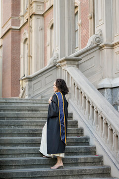 Berkeley graduate walking up classic campus staircase in gown