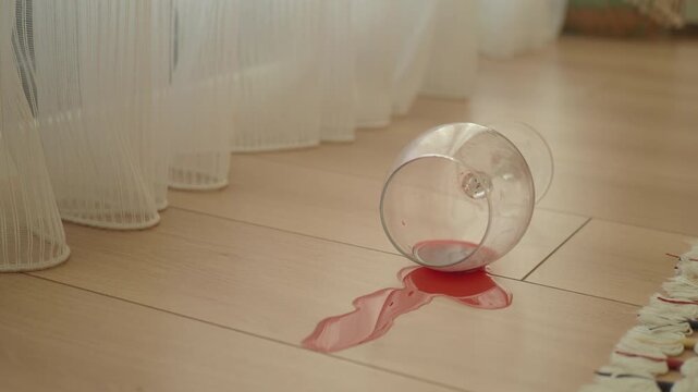 Glass spills wine on wooden floor in home setting