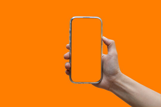 Hand holding white mobile phone with blank orange screen in orange background.