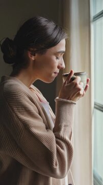 Woman enjoying coffee by the window &mdash; peaceful morning moment, vertical footage