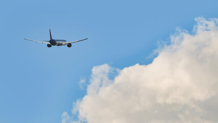 Obraz premium Commercial airplane flying away into a clear blue sky with fluffy white clouds, rear view