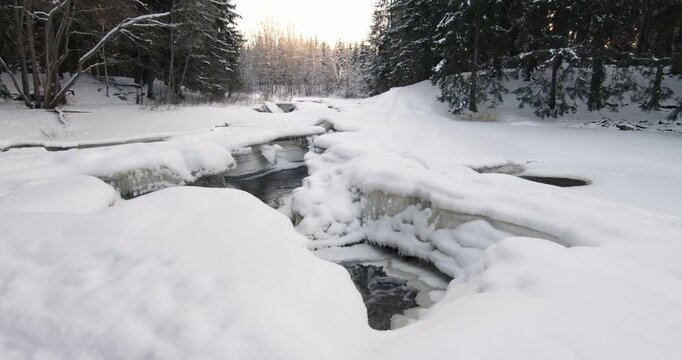 Tranquil, partially frozen river flowing through a snow-covered forest during winter, Matarinkoski, Vantaa, Finland, Europe.