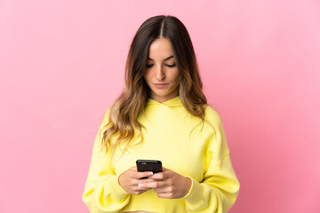 Fototapeta premium Young Romanian woman isolated on pink background using mobile phone