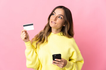 Young Romanian woman isolated on pink background buying with the mobile with a credit card while...