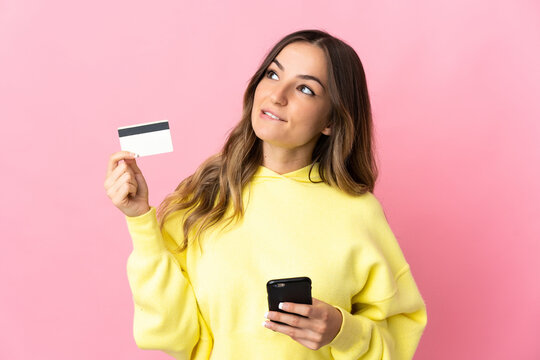Young Romanian woman isolated on pink background buying with the mobile with a credit card while thinking