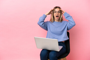 Young woman sitting on a chair with laptop over isolated pink background with surprise expression