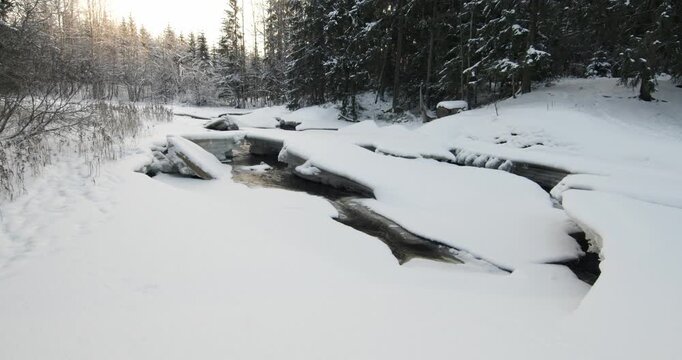 Tranquil, partially frozen river flowing through a snow-covered forest during winter, Matarinkoski, Vantaa, Finland, Europe.