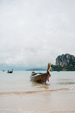 Long tail boat anchored at Railay West Beach with limestone cliffs