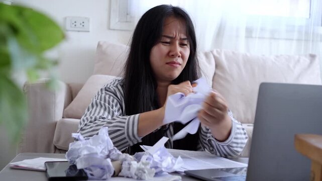 Frustrated Asian woman Tear the paper at home office desk, feeling stressed and overwhelmed by creative block or failed work project, struggling with deadline pressure and business failure.