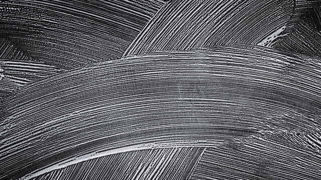 Abstract texture of white soap foam strokes on a black background. Concept of cleaning, car wash service, or hygiene. Top view of soapy suds pattern with curved lines and bubbles on dark surface.
