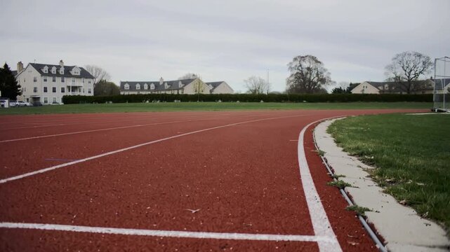 Track red rubber running with white lines on side, green grass and buildings in background on cloudy day featuring red track, rubber track, running