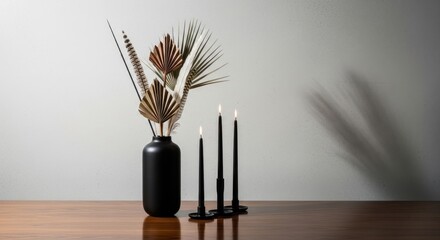 Naklejka premium Elegant matte black vase with dried botanical arrangement and three burning taper candles on a wooden table