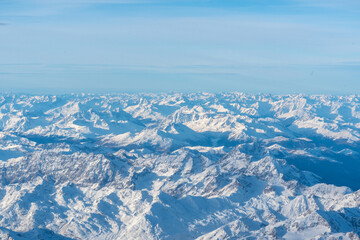 Plane view of mountains at sunrise, snow rock and blue cloudy sky aerial view