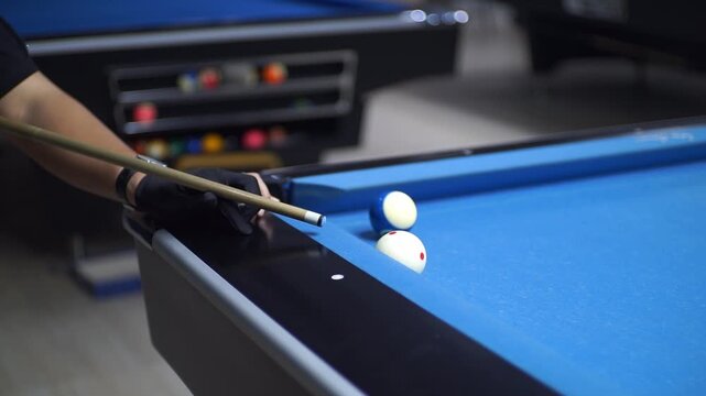 A player's gloved hand precisely aims a cue stick at the cue ball on a vivid blue billiard table, illustrating the focus and skill in a competitive game of pool
