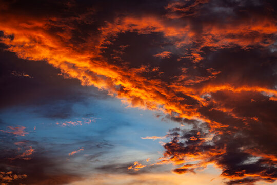 Dramatic fiery sunset sky with glowing orange clouds and deep blue atmosphere, creating a vivid natural background with intense colors and dynamic cloud formations.