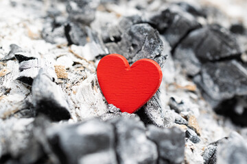 Obraz premium Red heart lying on cold grey ashes and charcoal. Concept of lost love or fading feelings. . Symbol of hope, rebirth and love .